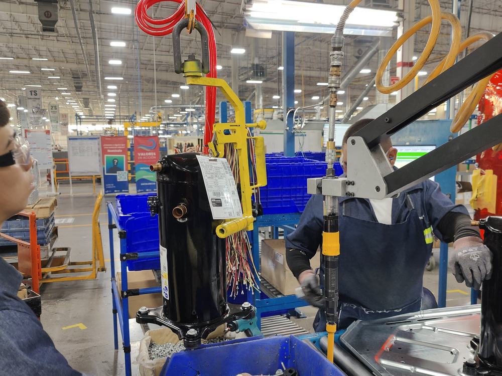 Operador maniobrando un compresor con el aditamento de izaje sobre la línea de ensamble