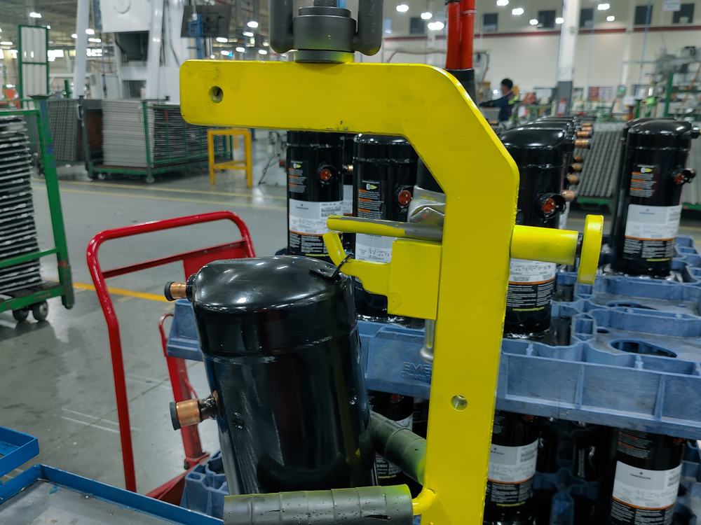 Aditamento de izaje amarillo suspendido sosteniendo un compresor sobre la línea de producción