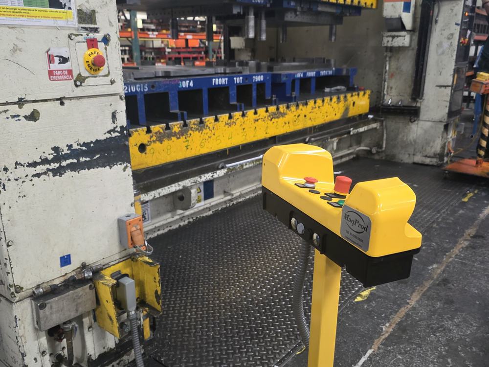 Pedestal de mando amarillo a dos manos instalado frente a una prensa industrial