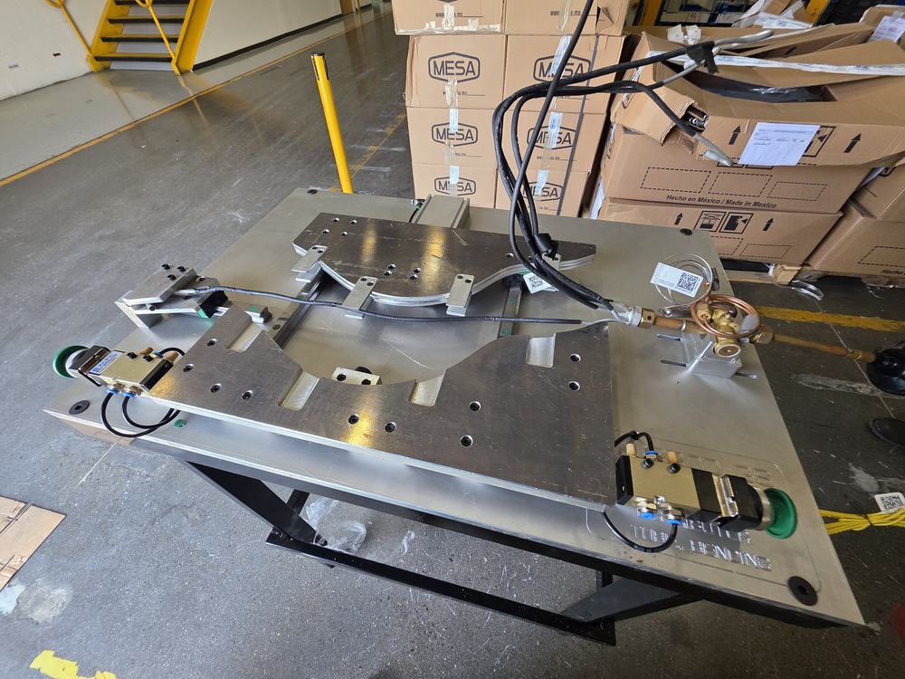 Fixture formador de tubo montado sobre mesa de trabajo en planta, con clamps y actuadores