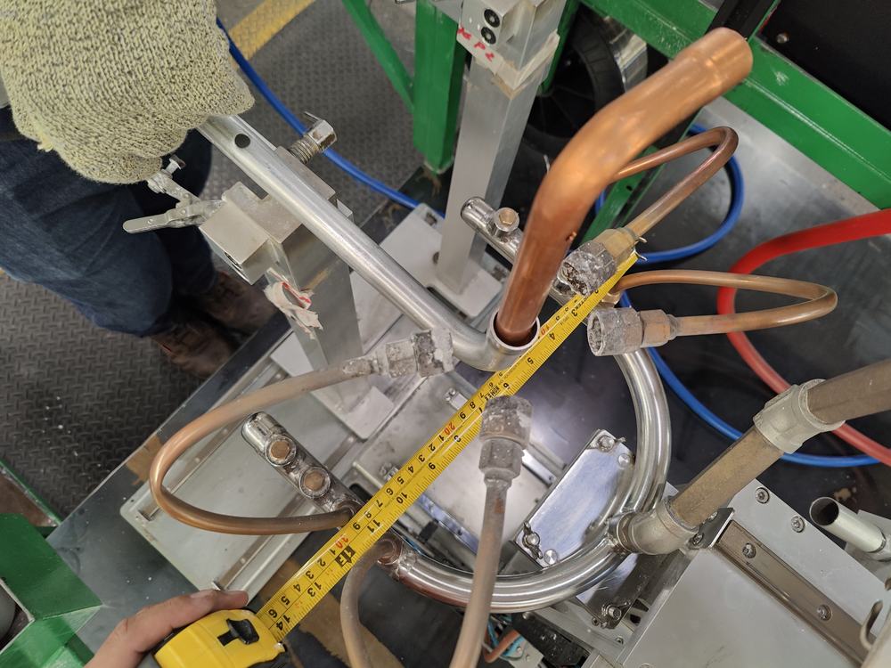 Manos midiendo con flexómetro un tubo de cobre montado en el fixture, para verificar la pieza