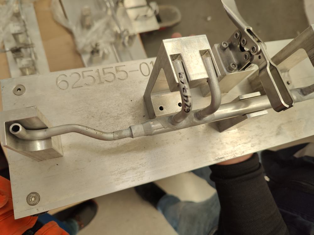 Manifold de tubo sujeto con clamps de palanca en un fixture de aluminio, con el número de parte grabado en la placa base
